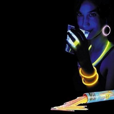 Pessoa com acessórios fluorescentes segurando um copo ao lado de palitos luminosos coloridos