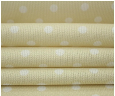 Tecido amarelo claro com bolinhas brancas empilhado e fundo bege com bolinhas brancas maiores