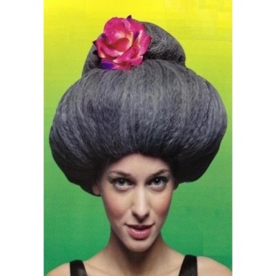 Mulher com peruca cinzenta volumosa e flor rosa em fundo verde-amarelo