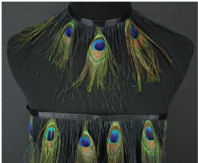 Conjunto de penas de pavão montadas em fitas pretas num manequim.