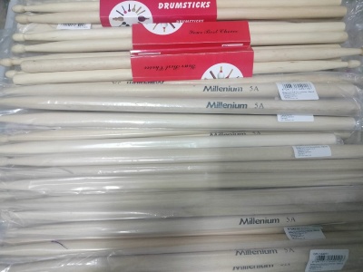 Baquetas de bateria de madeira clara com etiquetas Millenium 5A e Extra Quality, algumas embaladas em plástico.