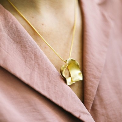 Colar dourado com pendente em forma de pétala numa camisa rosa