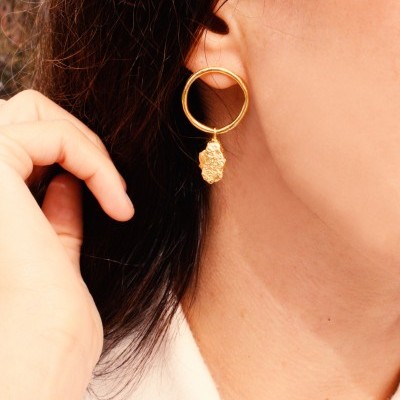 Brinco de argola dourada com pendente texturizado numa orelha feminina