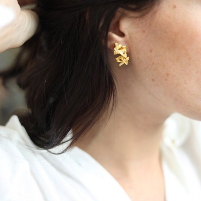 Brincos dourados entrelaçados no ouvido de uma mulher com camisa branca