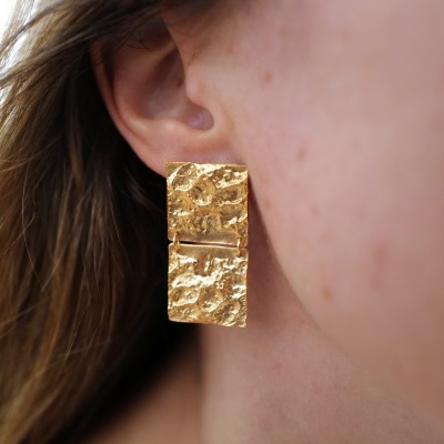 Brinco dourado retangular com textura rugosa na orelha
