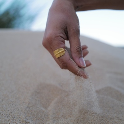 Mão segurando areia a cair em ambiente exterior com céu ao fundo