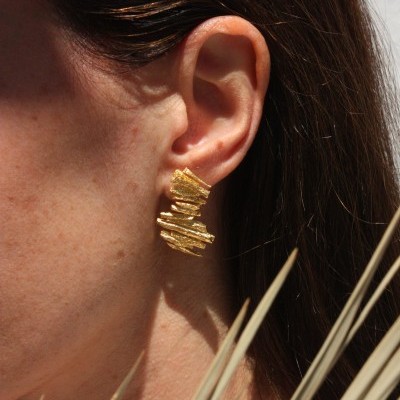 Brinco dourado texturizado numa orelha com cabelo castanho