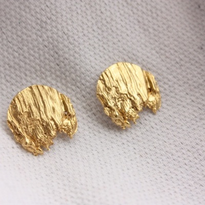 Brincos redondos dourados texturizados sobre tecido branco