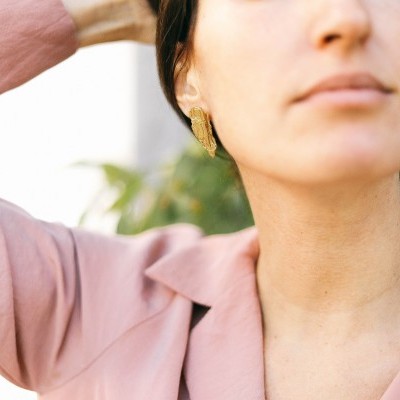 Brincos dourados em forma de folha usados por mulher com camisa rosa
