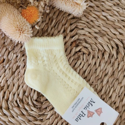 Meia amarela clara de malha com etiqueta branca sobre tapete de fibra natural com flores secas