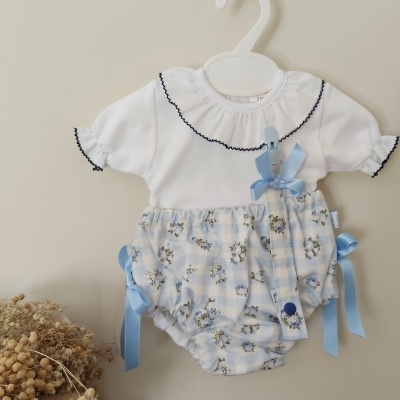 Roupa de bebé branca e azul com padrão floral pendurada num cabide