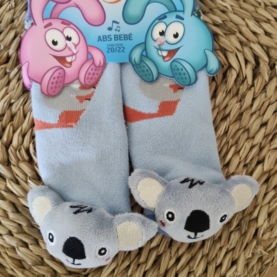 Meias de bebé azuis com peluches de coala cinza e etiqueta colorida com coelhos rosa e azul.