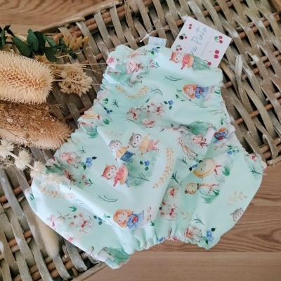 Culote de tecido com padrão infantil colorido sob superfície de vime e tag visível