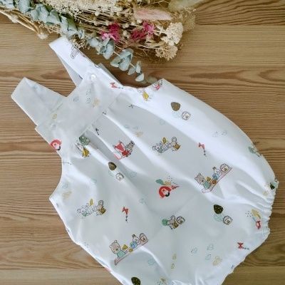 Macacão branco para bebé com estampados coloridos e alças largas sobre mesa de madeira clara