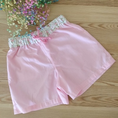 Calções rosa claro com padrão de pontos e cós floral sobre mesa de madeira com flores