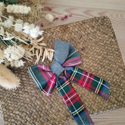 Carteira ou bolsa trançada natural com laço xadrez colorido sobre superfície de madeira clara e flores secas