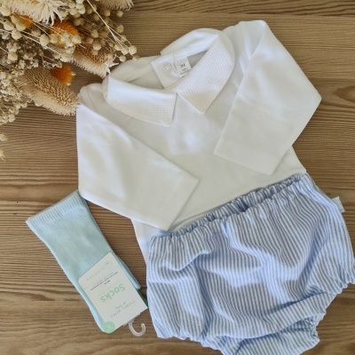 Conjunto de roupa de bebé branco com calções às riscas e meias azul claro sobre madeira clara