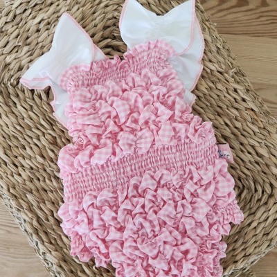 Body de bebé rosa com folhos e alças brancas sobre cesta de palha