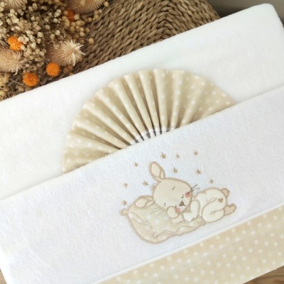Toalha de bebé branca com bordado de coelhinho e detalhes bege às estrelas sobre mesa de madeira