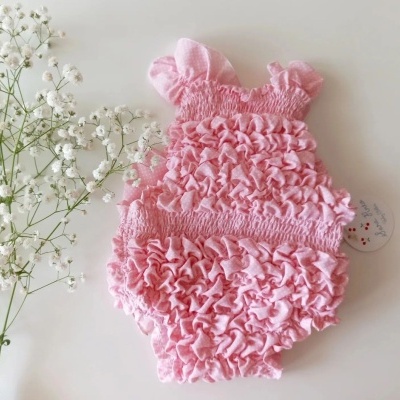 Body de bebé rosa com textura franzida ao lado de ramo de flores brancas