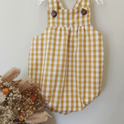 Jardineira bébé xadrez amarelo e branco com botões castanhos em cabide branco