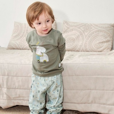Criança vestindo roupa verde e calças com padrão azul em frente a sofá bege.