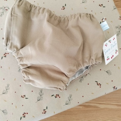Cueca para bebé bege claro com elásticos sobre tecido estampado com folhas e frutos.