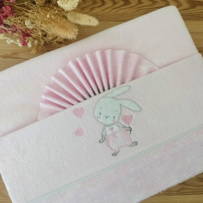 toalha de bebé cor-de-rosa com bordado de coelho e corações, detalhe plissado e flores secas ao fundo