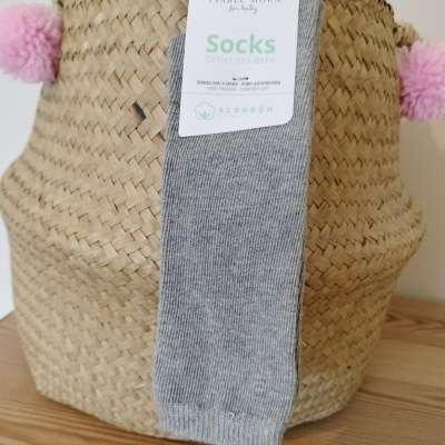 Meias cinzentas para bebé com etiqueta penduradas em cesto de palha com pompons cor-de-rosa