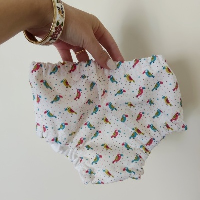 Cueca infantil branca com padrão de pássaros coloridos segurada por mão com pulseira