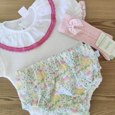 Conjunto de roupa de bebé com body branco, calções florais e meias cor-de-rosa com laço