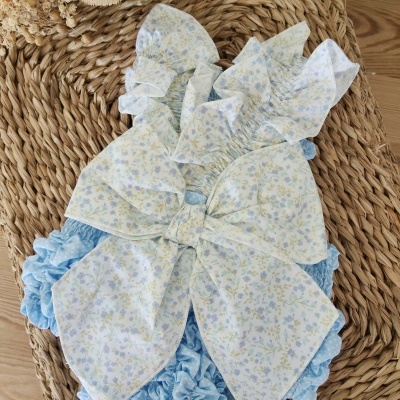 Vestido azul claro floral com laço grande sobre tapete de palha trançada