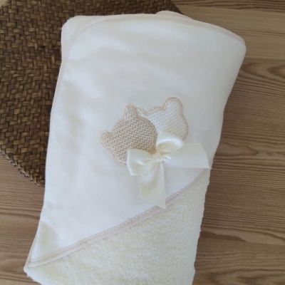 Toalha de bebé branca com ursinhos e laço sobre madeira clara e tapete castanho