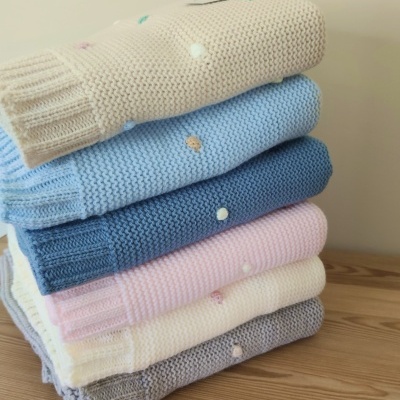 Seis camisas de malha coloridas dobradas empilhadas sobre uma mesa de madeira clara