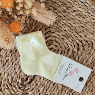 Meia amarela clara com laço e etiqueta branca sobre esteira natural com decoração seca
