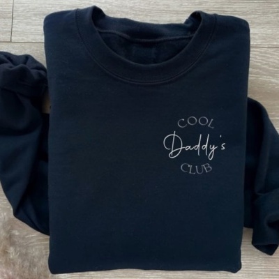 T-shirt preta de manga comprida dobrada com texto branco no peito sobre chão de madeira clara