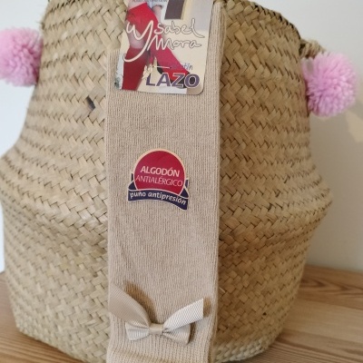 Meias de algodão bege claro com laço e etiqueta penduradas em cesta de palha com pompons cor-de-rosa