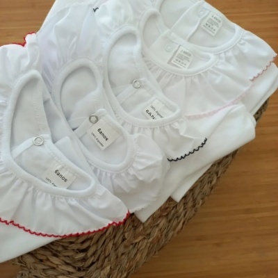 Cinco bodies brancos para bebé com gola frisada e bainha decorativa colorida, marca GANT'S, sobre cesta de vime