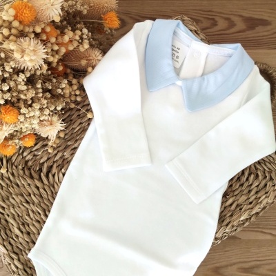Body de bebé branco com gola azul clara e flores secas ao lado