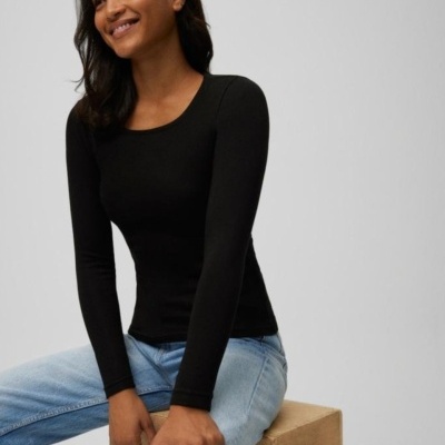 Mulher com top preto manga comprida e jeans azul claro sentada numa caixa de madeira