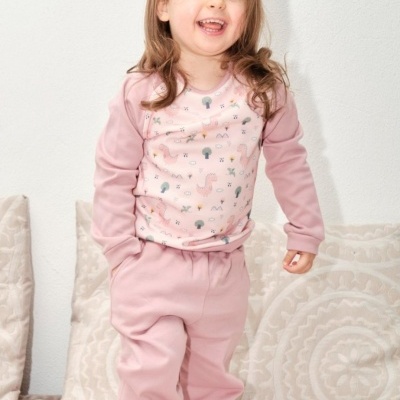 Criança com pijama rosa com motivos pequenos e coloridos, em ambiente interior com almofadas.