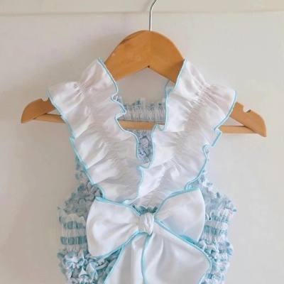 Body de bebé branco e azul com gola e laço, pendurado num cabide de madeira