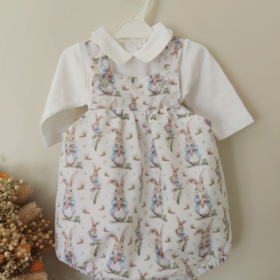 Conjunto de bebé com macacão estampado de coelhos e camisa branca pendurado