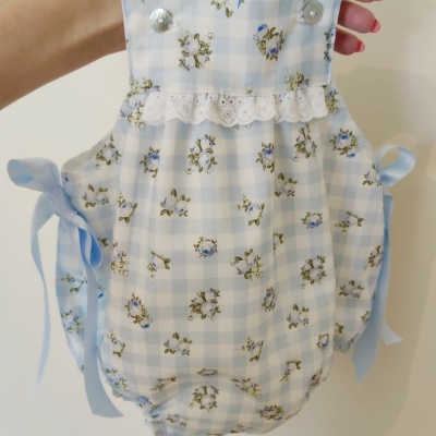 Macacão de bebé azul claro e branco com padrão de xadrez e flores, renda branca e fitas azuis