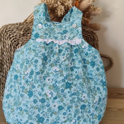 Babygrow azul com flores e botões brancos em cadeira de vime com flores secas