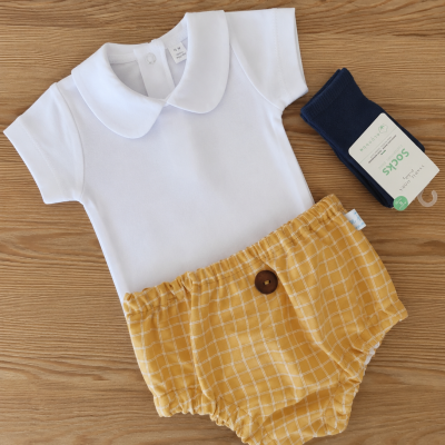 Conjunto de roupa de bebé branco, amarelo e azul sobre superfície de madeira