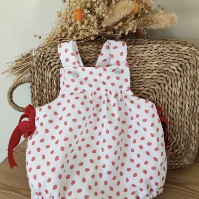 Roupinha de bebé branca com padrão de morangos vermelhos e laços vermelhos