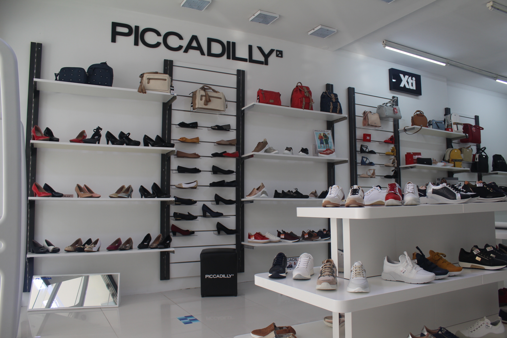 Interior de loja de calçado com sapatos e bolsas expostas em prateleiras e mesas