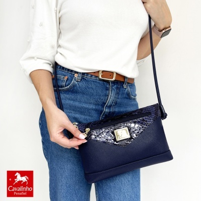 Mala de ombro azul escuro com textura de pele de cobra e fecho dourado, em modelo com camisola branca e jeans azuis