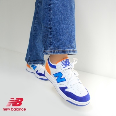 Ténis brancos e azuis New Balance com detalhes laranja em chão branco